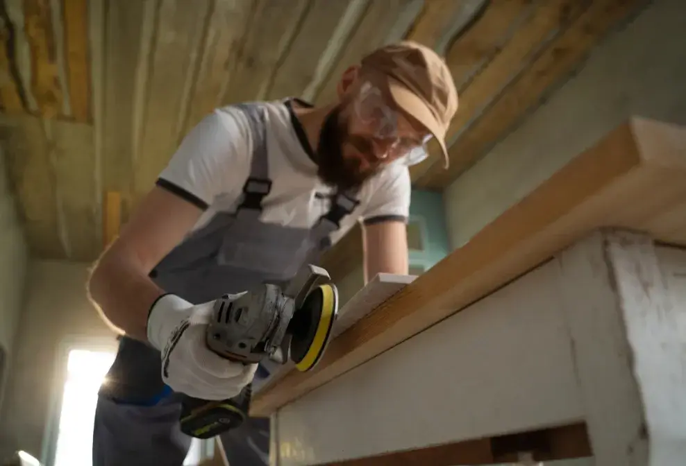 Carpenter sanding a wood plank with an electric sander, part of custom wood finishing by Jorge Carpentry & Tile Services.