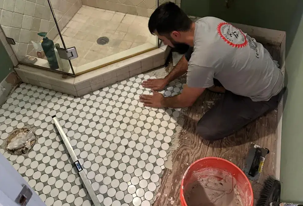 Contractor installing round tiles on a bathroom floor near a glass shower