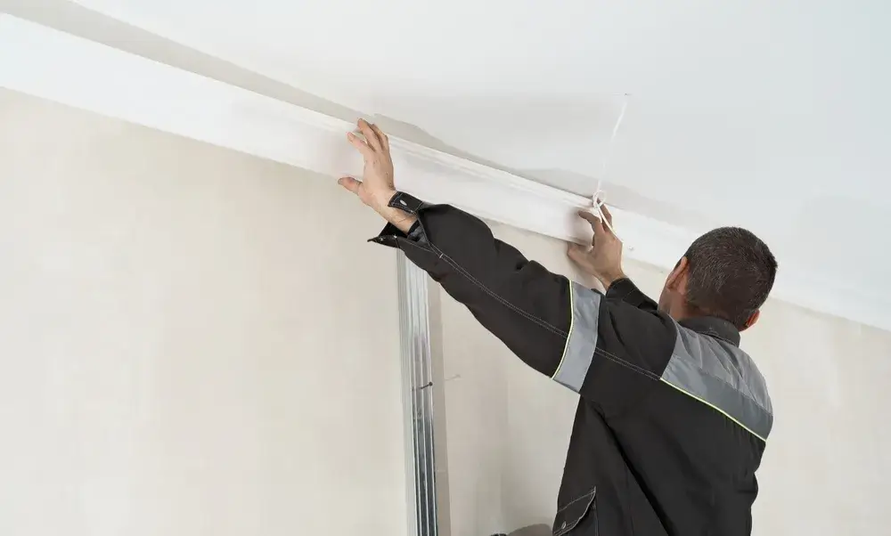 Carpenter installing crown molding on a white ceiling