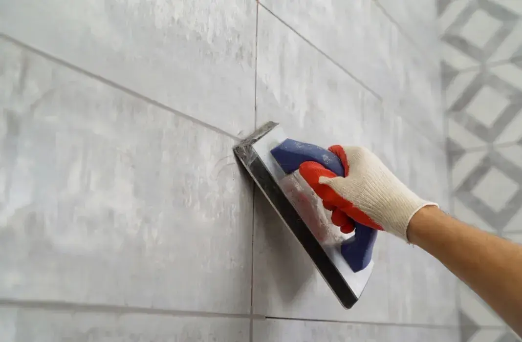 Worker applying grout to wall tiles with a float tool