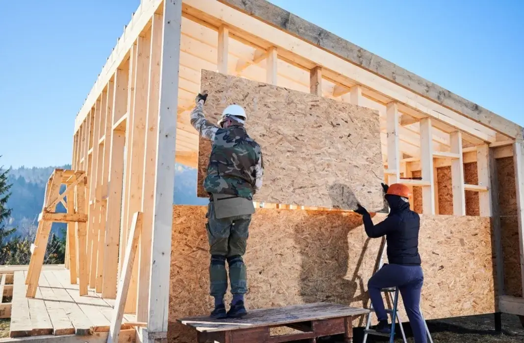Construction team installing sheathing on wooden house framing