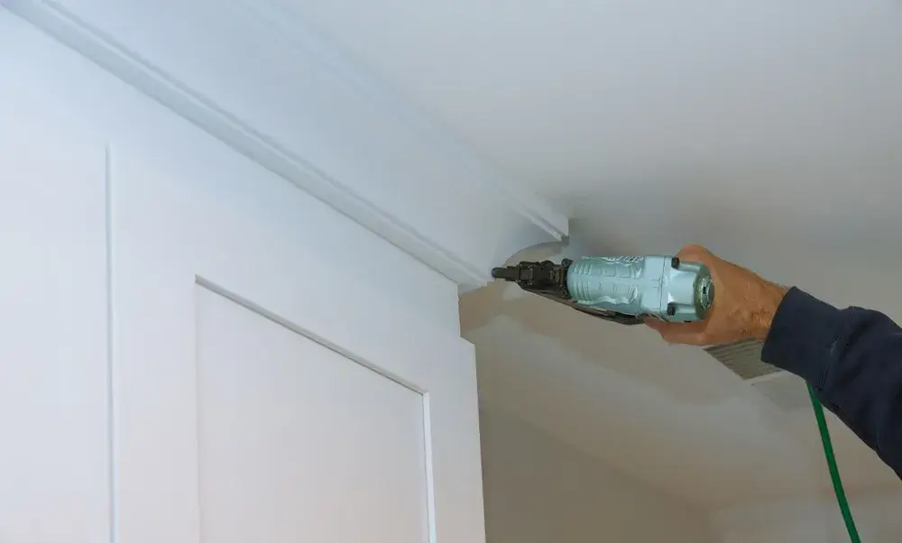 Trim being nailed to ceiling corner using power nailer